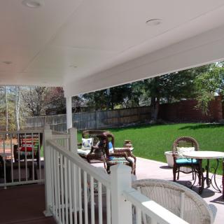 A view of a backyard patio with outdoor furniture under a covered porch overlooking a green lawn.