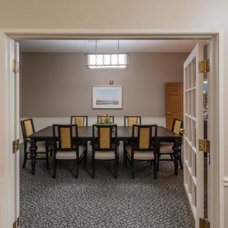 A well-lit dining or conference room with a large table and several chairs, decorated in a neutral color scheme.