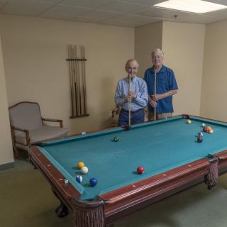 Two people standing next to a pool table in a leisure room.