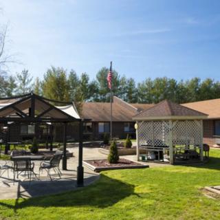 A sunny outdoor area with a gazebo, patio furniture, and a building in the background.