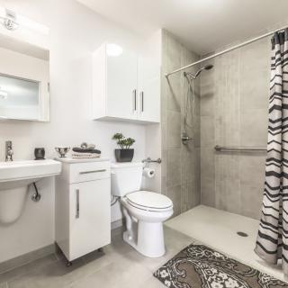 A modern, minimalist bathroom with a white color scheme featuring a shower, toilet, and sink.