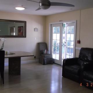A living room with a table, chairs, and an armchair, featuring a mirror on the wall and a ceiling fan.