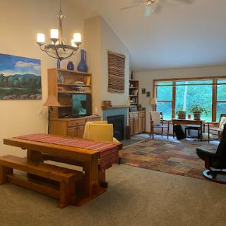 A cozy living space featuring a dining area with wooden furniture, a chandelier, and a large window bringing in natural light.