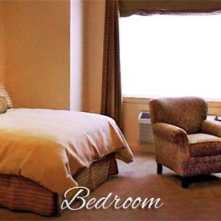 A cozy bedroom with a bed and an armchair near a window.