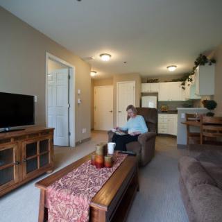 A cozy living room with a television, sofa, and coffee table, leading into a small kitchen area.