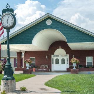 A quaint building with a clock and an American flag stands amidst a lush green lawn under a partly cloudy sky.