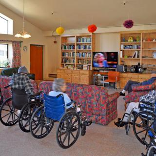 Elderly residents in a nursing home are watching television together in a communal living room.
