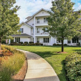A sunny day view of an apartment building surrounded by lush greenery and a winding pathway.