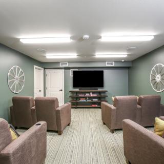 A cozy home theater room with armchairs, a large television, and ambient lighting.