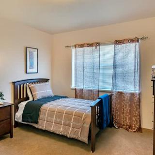 A cozy bedroom with a single bed, nightstand, and window with curtains.