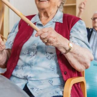 Elderly individuals participating in a group exercise session using sticks.