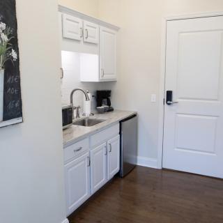 A compact kitchen area featuring white cabinets, a coffee maker, and a sink.
