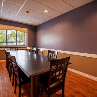 A spacious conference room with a large meeting table and chairs, featuring a window and wooden flooring.
