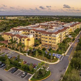 Aerial view of a large apartment complex surrounded by greenery and parking lots at sunset.