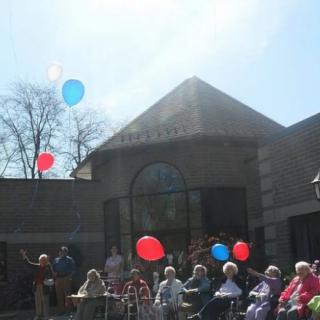 A group of people enjoying a sunny day outside with balloons in front of a building.