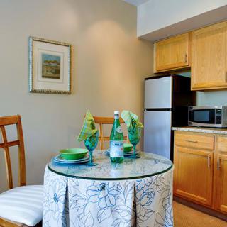 A cozy kitchen and dining area with a round table set for two, featuring wooden cabinetry and modern appliances.