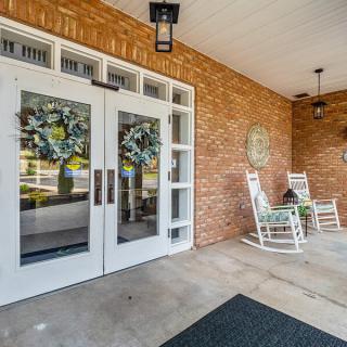 A welcoming porch with double glass doors adorned with wreaths and two white rocking chairs.