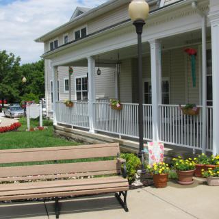 A charming porch with flower pots and a nearby bench under a clear sky.