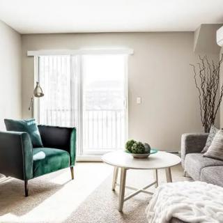 A modern and minimalist living room with abundant natural light, featuring a green armchair, a sofa, and a round coffee table.