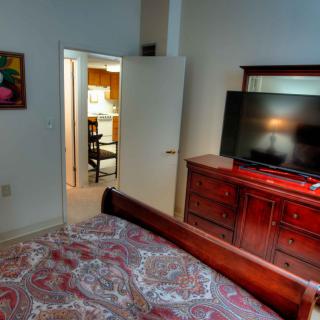 A cozy bedroom featuring a large bed, wooden dresser with a TV on top, and an open door leading to another room.