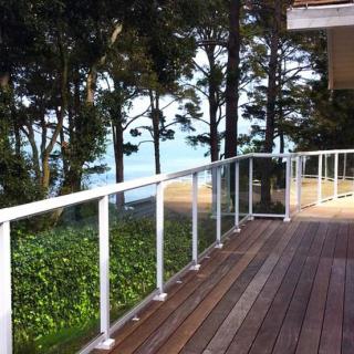 A serene wooden deck with a glass railing overlooks the ocean, surrounded by lush trees.