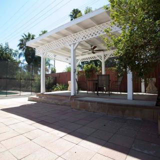 A sunny backyard with a white pergola providing shade over a tiled patio area.