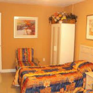 A cozy bedroom with orange walls, a single bed featuring colorful bedding, and decorative artwork on the walls.