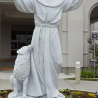 A statue depicting a religious figure with arms raised, accompanied by a sheep.
