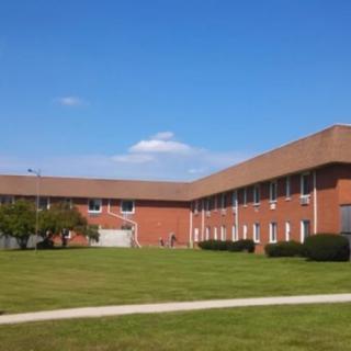 A large brick school building with a well-maintained lawn under a clear blue sky.