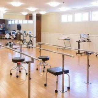 A well-equipped physical therapy room with various exercise machines and parallel bars.