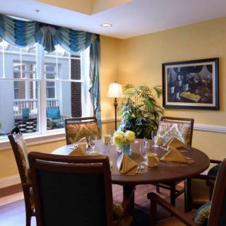 A cozy dining room with a round table set for four, featuring elegant decor and large windows allowing natural light in.