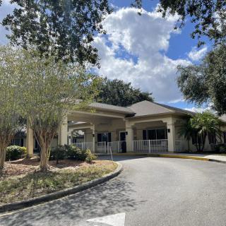 A building with a driveway surrounded by trees under a partly cloudy sky.