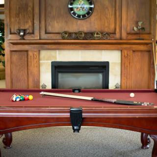 A cozy recreation room featuring a pool table with billiard balls and a cue stick, set against a wooden-paneled fireplace.