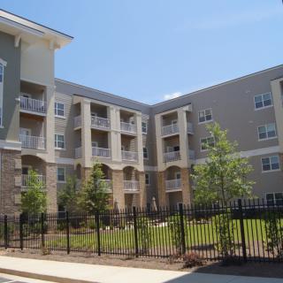 A modern apartment building with landscaped greenery and a surrounding fence.