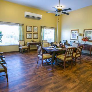 A cozy dining room with wooden floors, a dining table, and chairs, featuring windows and a ceiling fan.