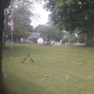 A peaceful park scene featuring a flag, grassy area, and surrounding trees.