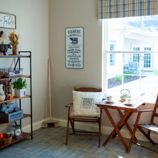 A cozy living room corner with a wooden chair, a small table, and a decorative shelf beside a large window.