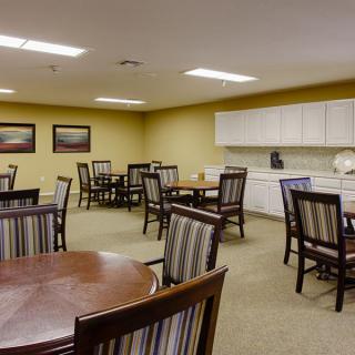 A dining room with tables and chairs, featuring a kitchen area in the corner and art on the walls.