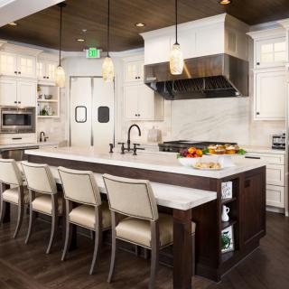 A modern kitchen featuring a large island with bar stools, white cabinets, and stainless steel appliances.