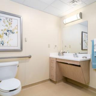 A clean and modern bathroom with a toilet, sink, mirror, and wall art.