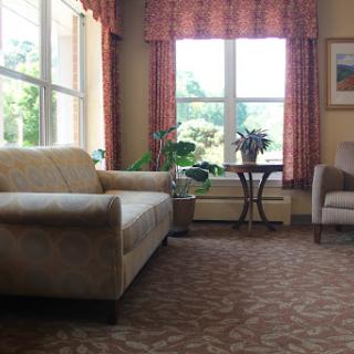 A cozy living room featuring a sofa, an armchair, and a small table beside a window with natural light streaming in.