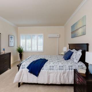 A modern bedroom with a neatly made bed, artwork on the wall, and a large window with shutters.