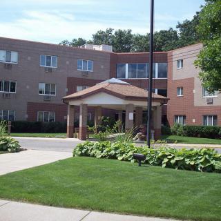 A view of a multi-story apartment building with a landscaped entrance and green lawn.