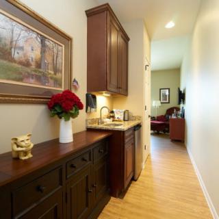 A narrow hallway featuring a kitchenette with wooden cabinets and a vase of flowers, leading to a living area.