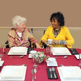 Two elderly women enjoying a conversation at a dining table, sharing smiles and companionship.