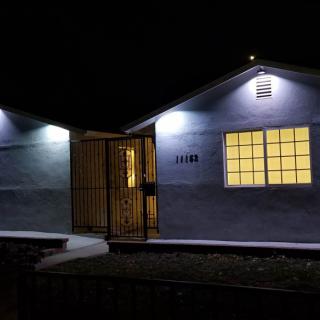 A small house illuminated at night with visible windows and a gated entrance.