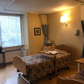 A comfortable hospital patient room featuring two beds and natural light from a window.