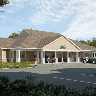 A suburban building with a parking lot and people near the entrance on a clear day.