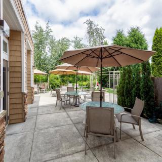A cozy outdoor patio with tables and chairs under large umbrellas, surrounded by lush greenery.