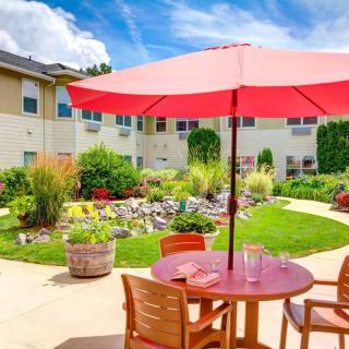A sunny courtyard with a patio table and umbrella surrounded by a well-maintained garden.